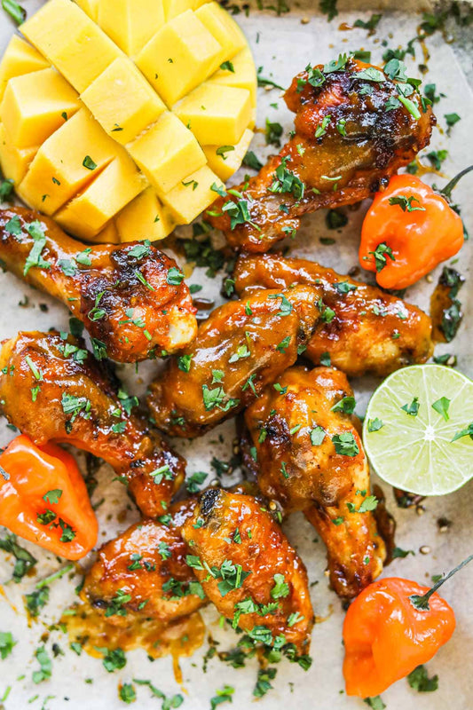 Crispy chicken wings coated in glossy mango habanero sauce, garnished with green onion and lime wedges
